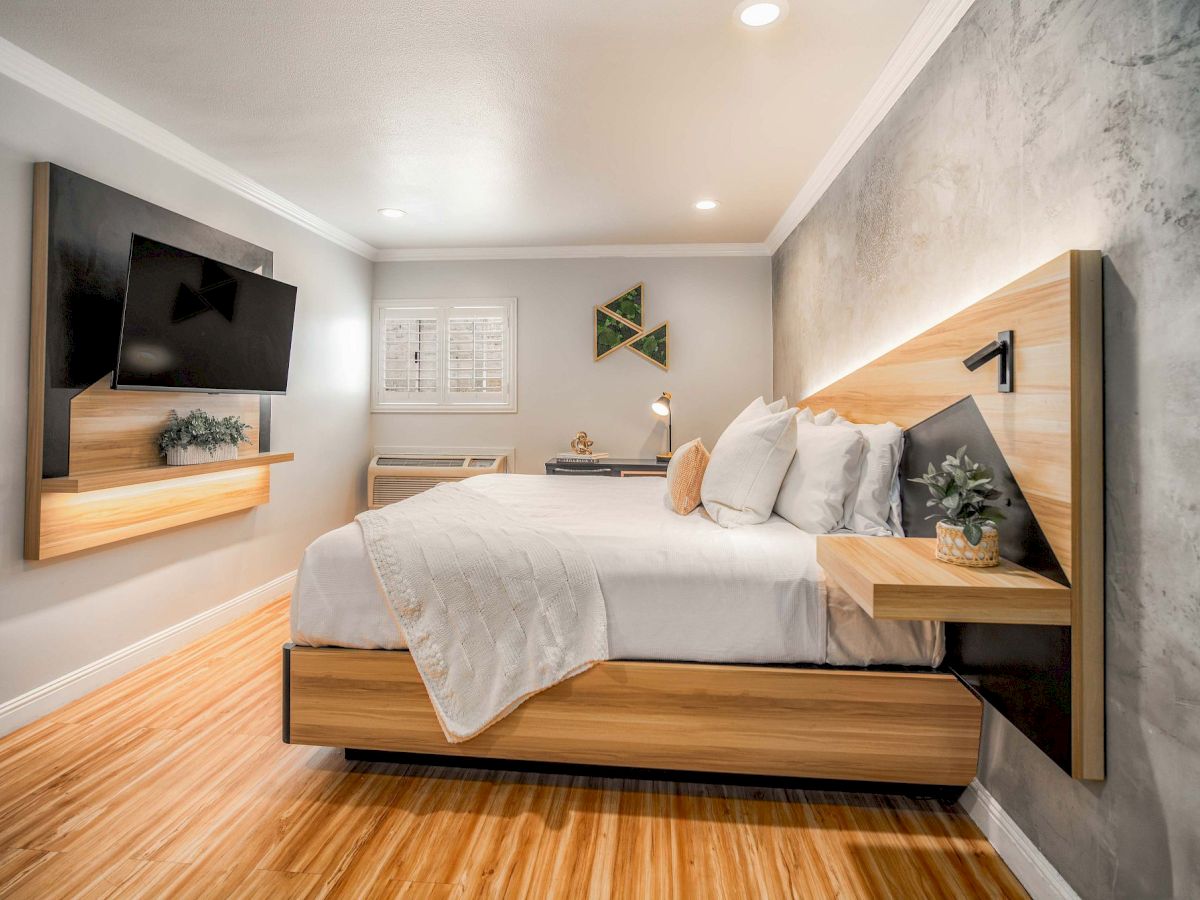 A modern hotel room with a large bed, mounted TV, and decorative elements.