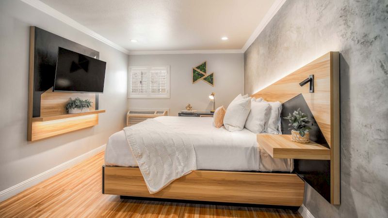 A wide-angle view of a modern hotel room with a large bed, mounted TV, and recessed lighting.