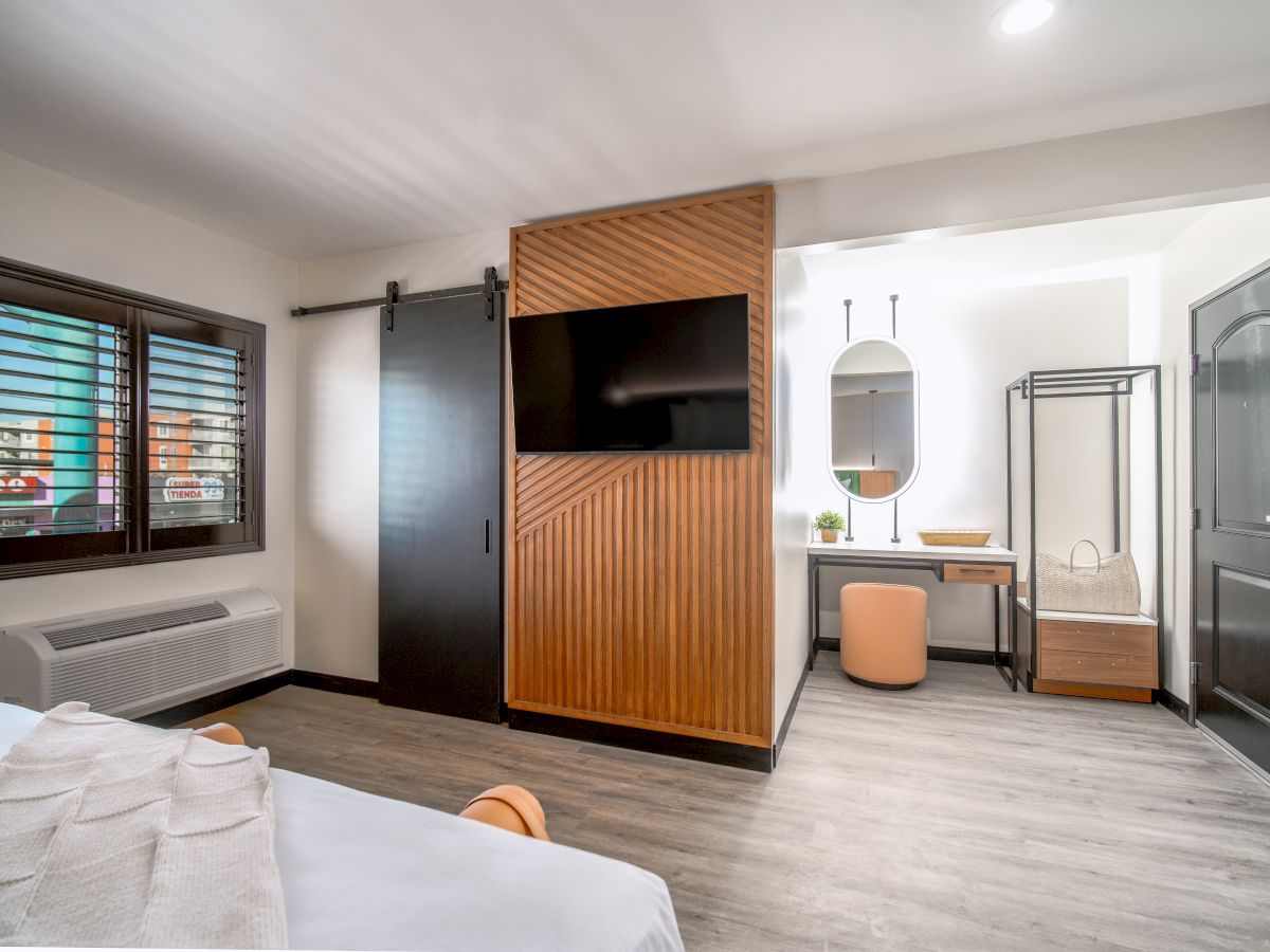 A modern hotel room with a bed, TV, desk, and window.