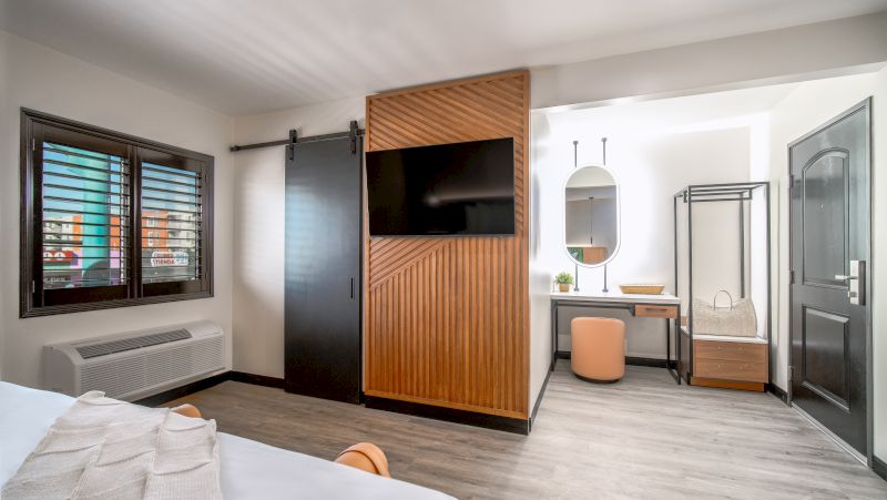 A modern hotel room with a bed, TV, desk, and window.