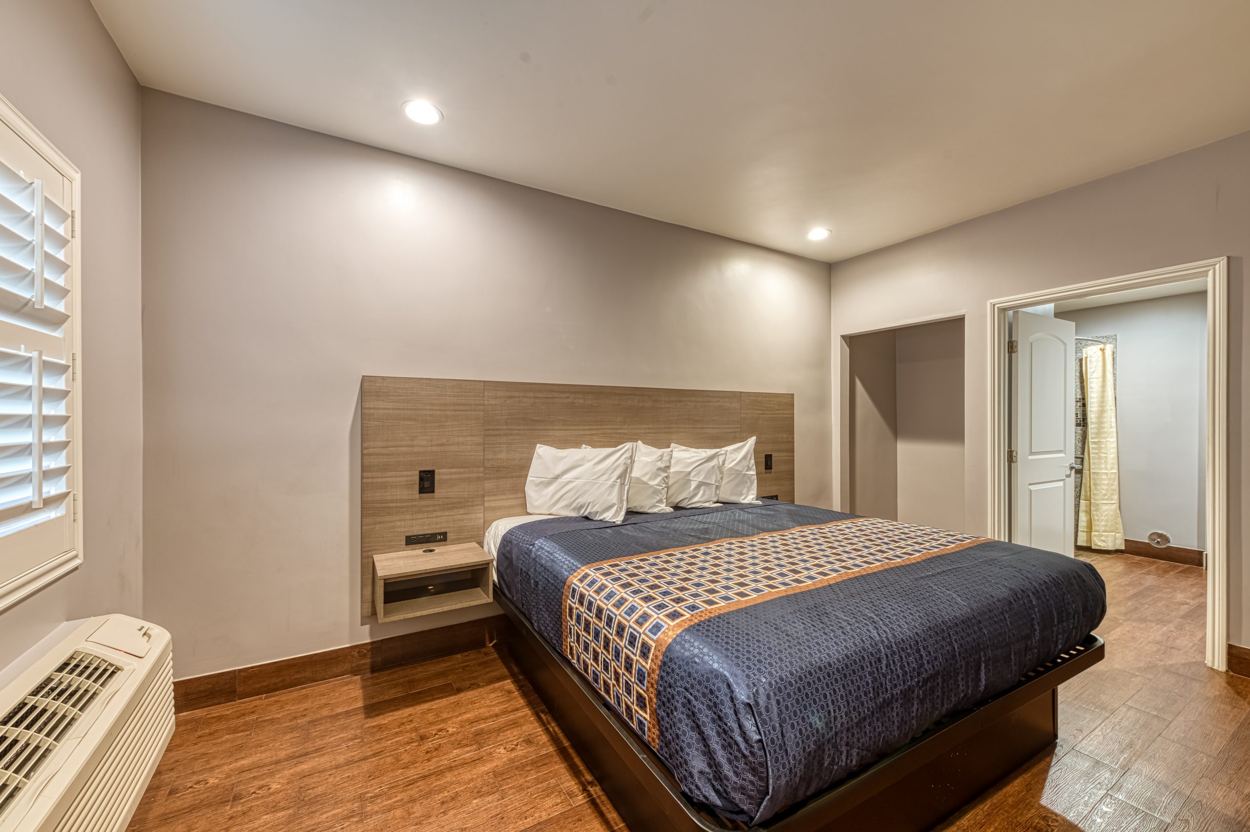 A wide view of a hotel room with a bed, window, and doorway.
