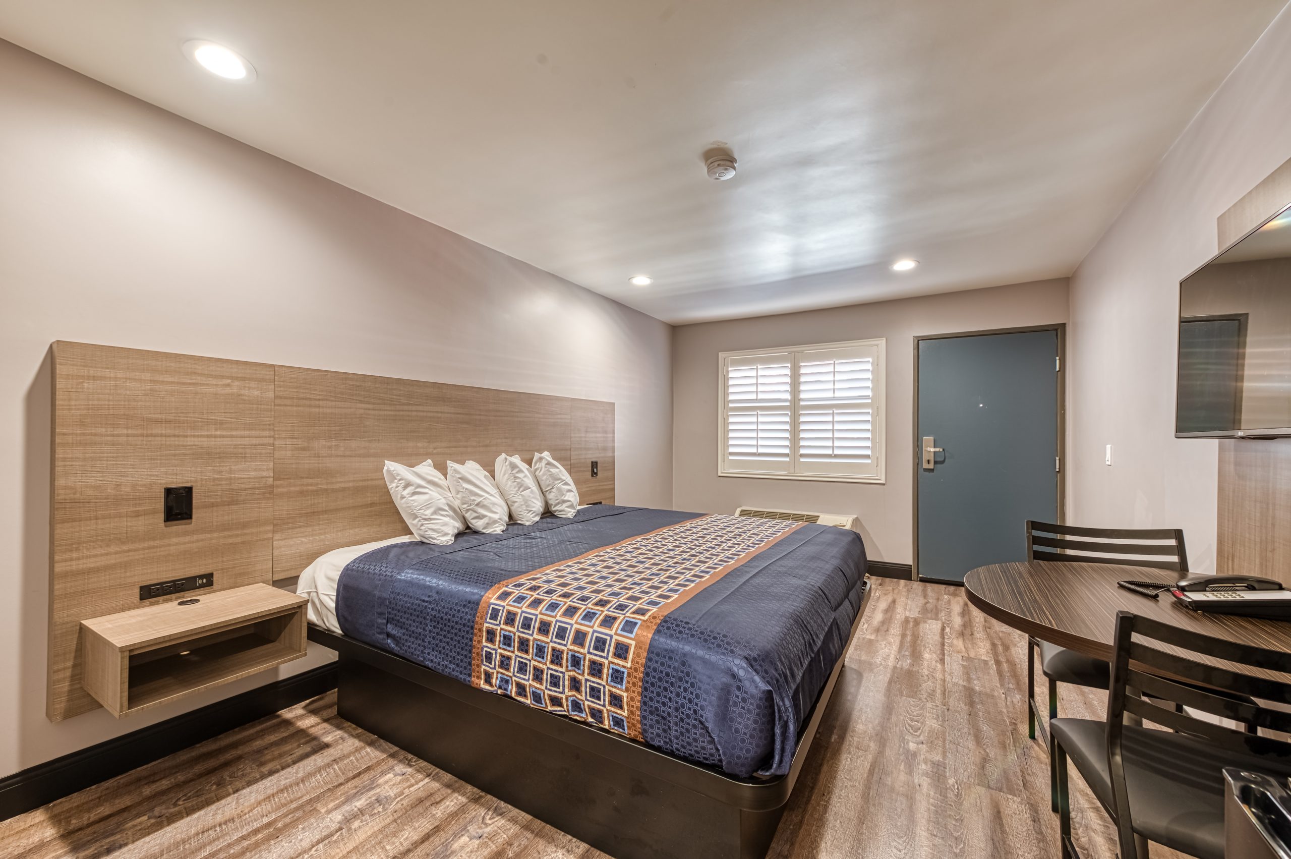 A hotel room with a bed, table, chairs, window, and door.