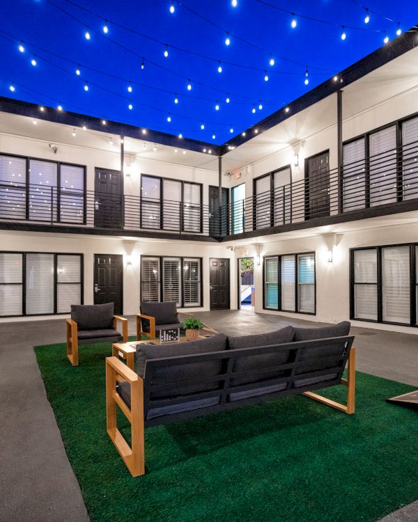 A hotel courtyard with seating area, string lights, and balcony.