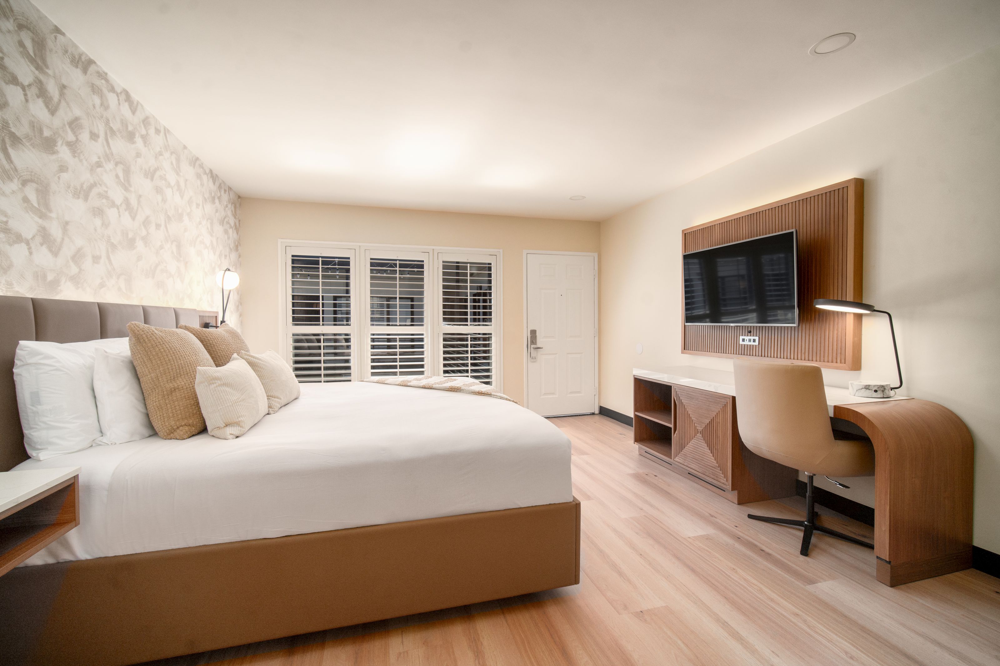 A wide-angle view of a hotel room with a large bed, desk, TV, and window.