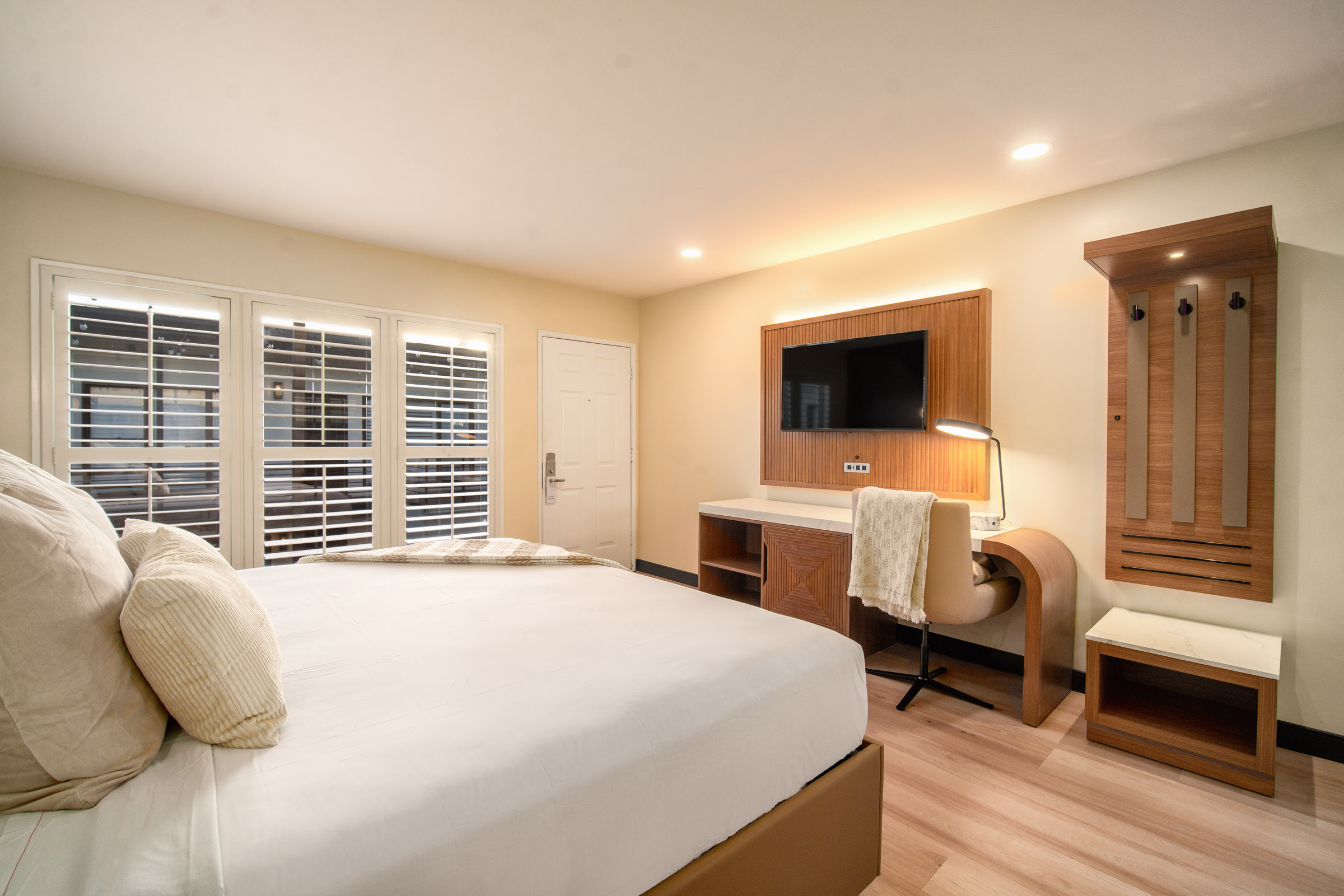 A hotel room with a king-sized bed, desk, TV, closet, and window.