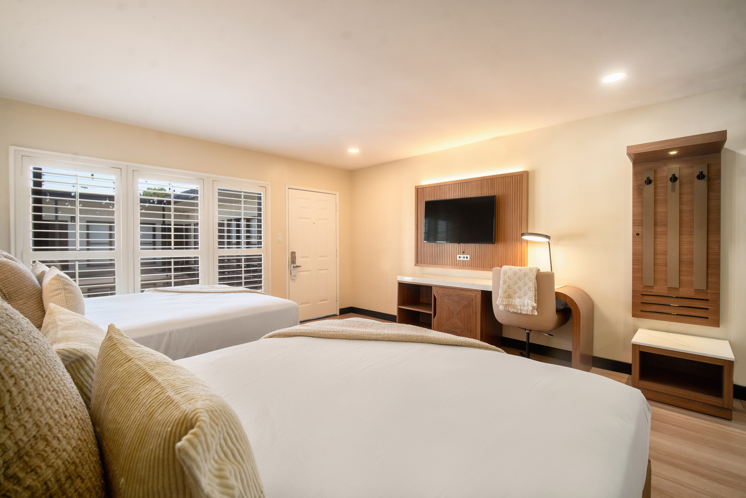 A hotel room with two beds, a desk, a TV, and a window.