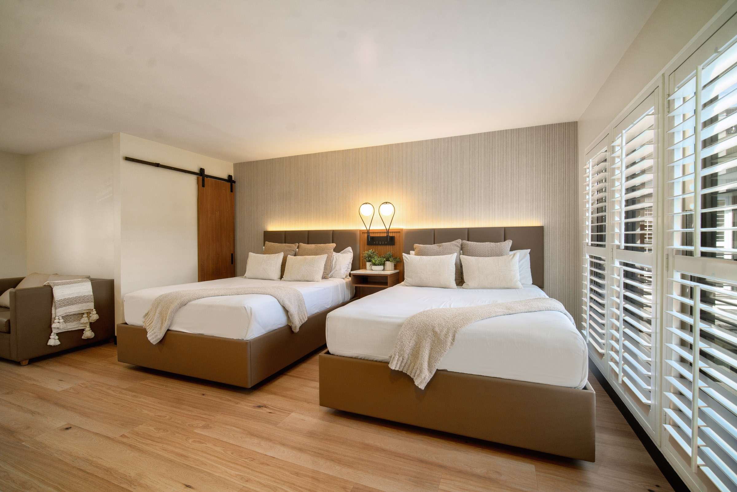 A wide view of a hotel room with two beds, a window with blinds, and modern furniture.