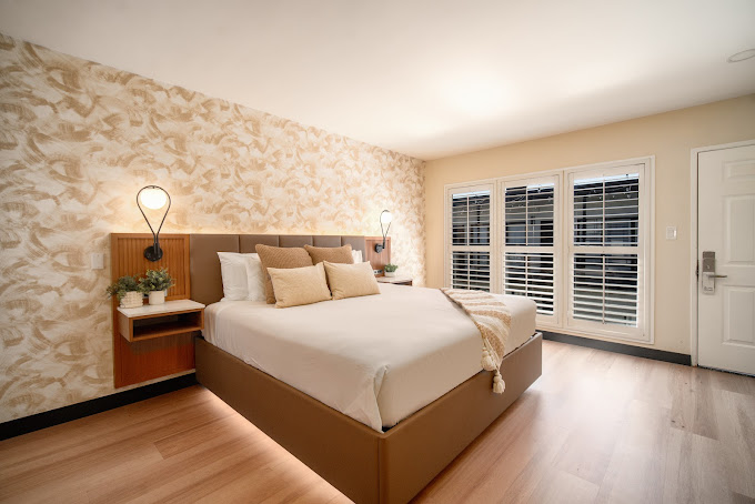 A wide-angle view of a hotel room with a large bed, two nightstands, and a window.