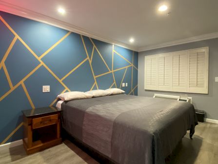 A wide view of a guest room with a blue accent wall featuring gold geometric patterns, a gray bed, and a wooden nightstand.