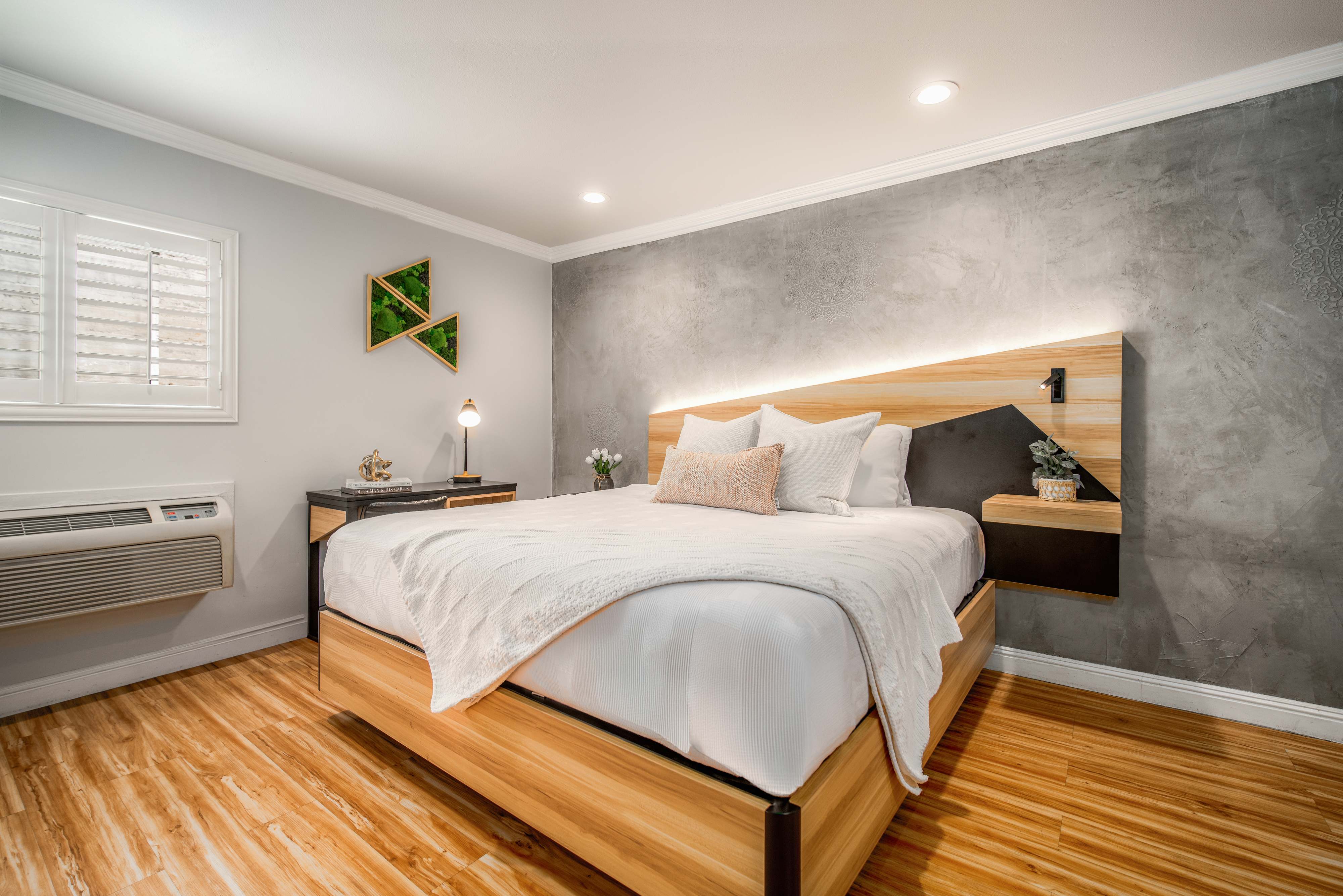 A clean and modern hotel room with a large bed, nightstand, and artwork on the wall.